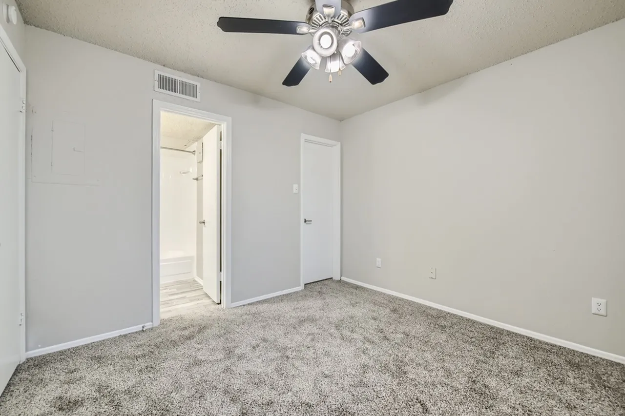 Primary bedroom, gray carpet flooring, ceiling fan with light fixture, ensuite bathroom entry