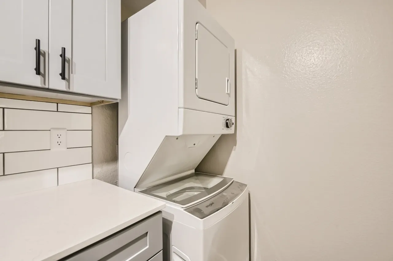 Laundry room, stacked washer and dryer, white cabinetry, subway tile backsplash