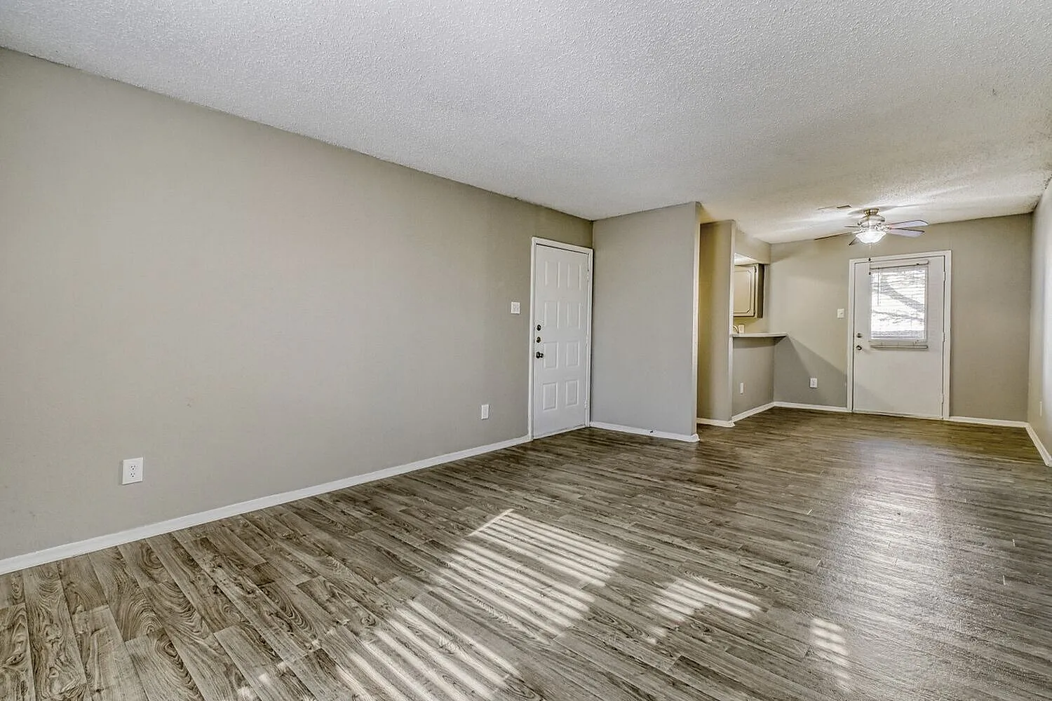 Living room, wood-style plank flooring, ceiling fan, entry door, neutral walls