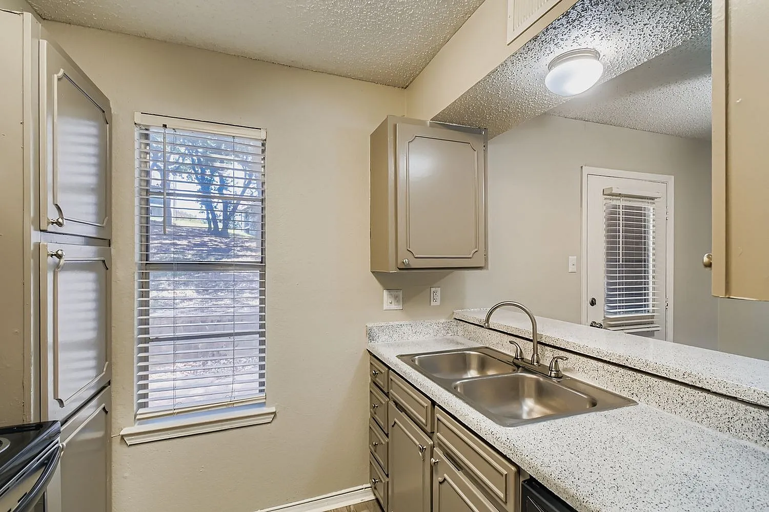 Kitchen with gray cabinetry, speckled quartz countertops, stainless sink, window, laundry appliances