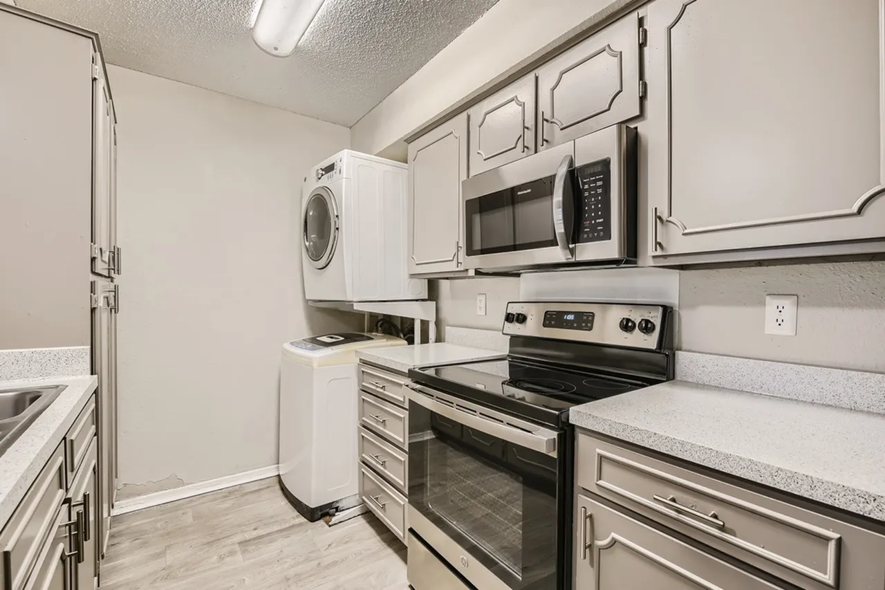 Kitchen and laundry area, white shaker cabinetry, stainless appliances, quartz countertops, wood-style plank flooring