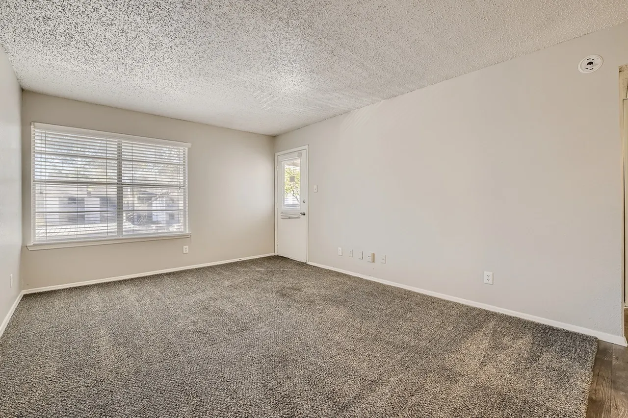 Empty bedroom, brown carpeting, large windows with shutters, textured ceiling