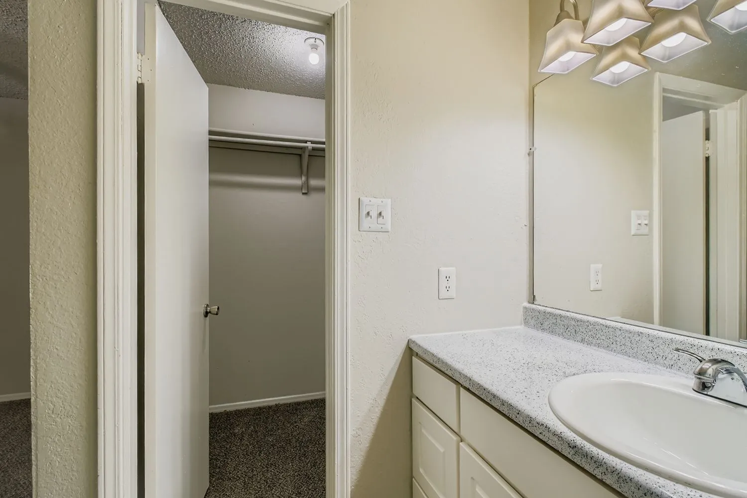 Bathroom, white vanity cabinet, speckled gray countertops, mirror, walk-in closet