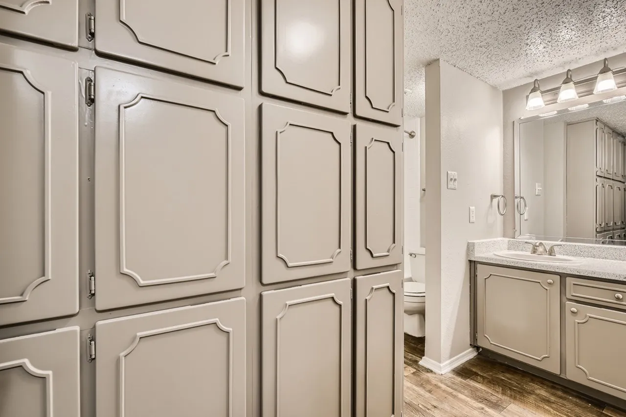 Primary bathroom, cream cabinetry, quartz countertops, large mirror, wood-style plank flooring