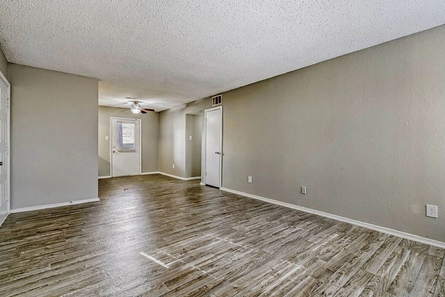 Living room with wood-style plank flooring, beige walls, ceiling fan, entry door