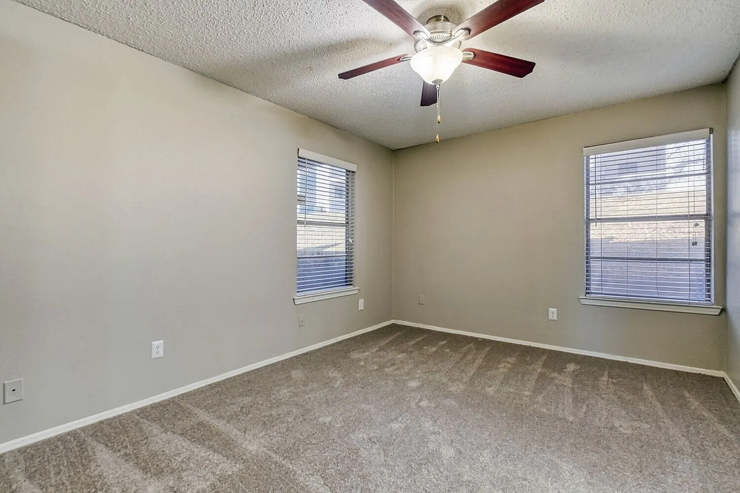 Bedroom, gray carpet flooring, two windows with blinds, ceiling fan with light fixture
