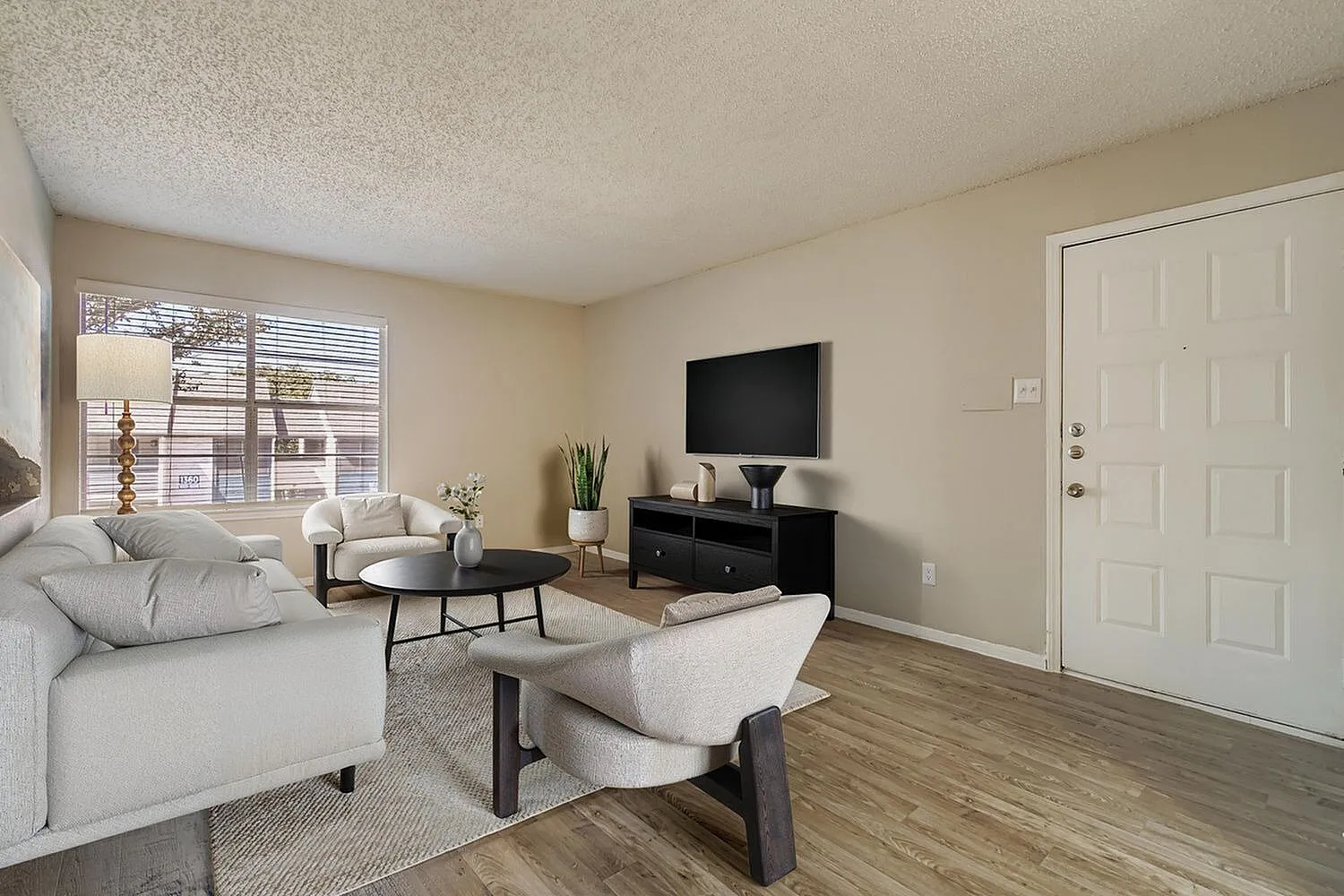 Living room with wood-style plank flooring, white sofa, upholstered accent chair, black entertainment console, flat screen television