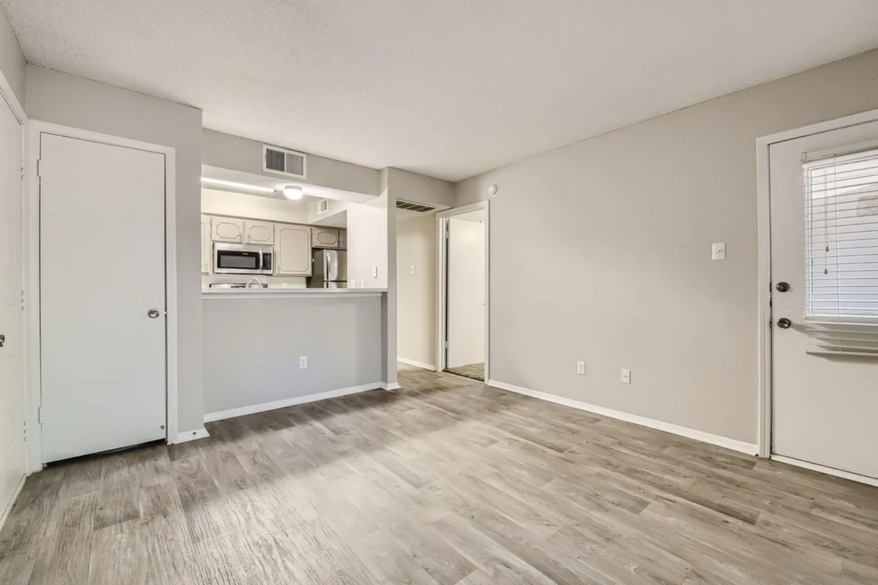 Open living area, wood-style plank flooring, gray painted walls, kitchen with white cabinetry and stainless appliances