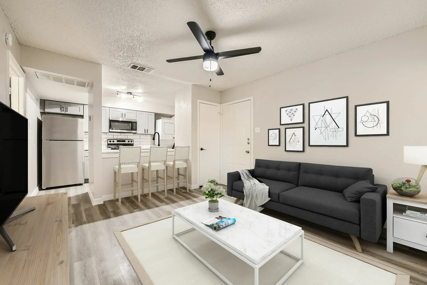 Living room and kitchen, wood-style plank flooring, black ceiling fan, cream shaker cabinetry, stainless appliances