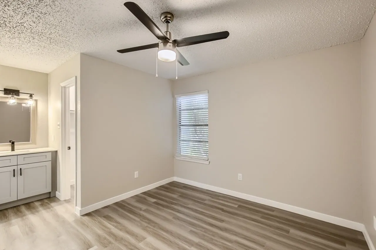 Primary bedroom, wood-style plank flooring, ceiling fan with light, window with blinds