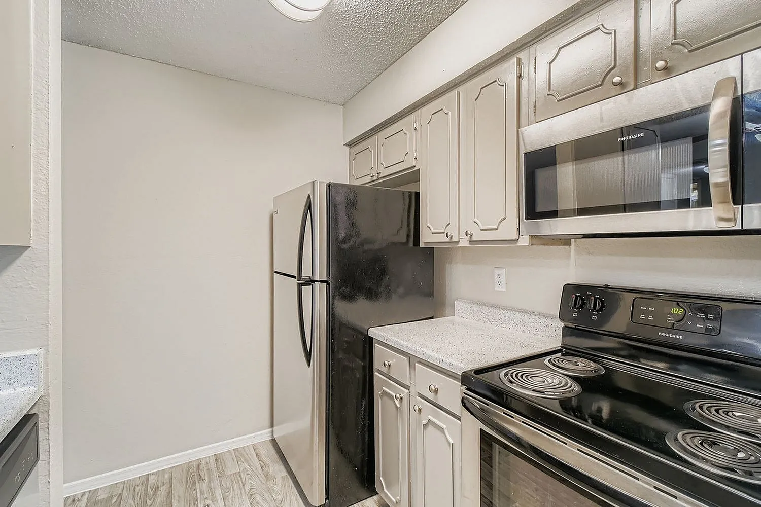 Kitchen, cream cabinetry, light countertops, black stove, stainless microwave