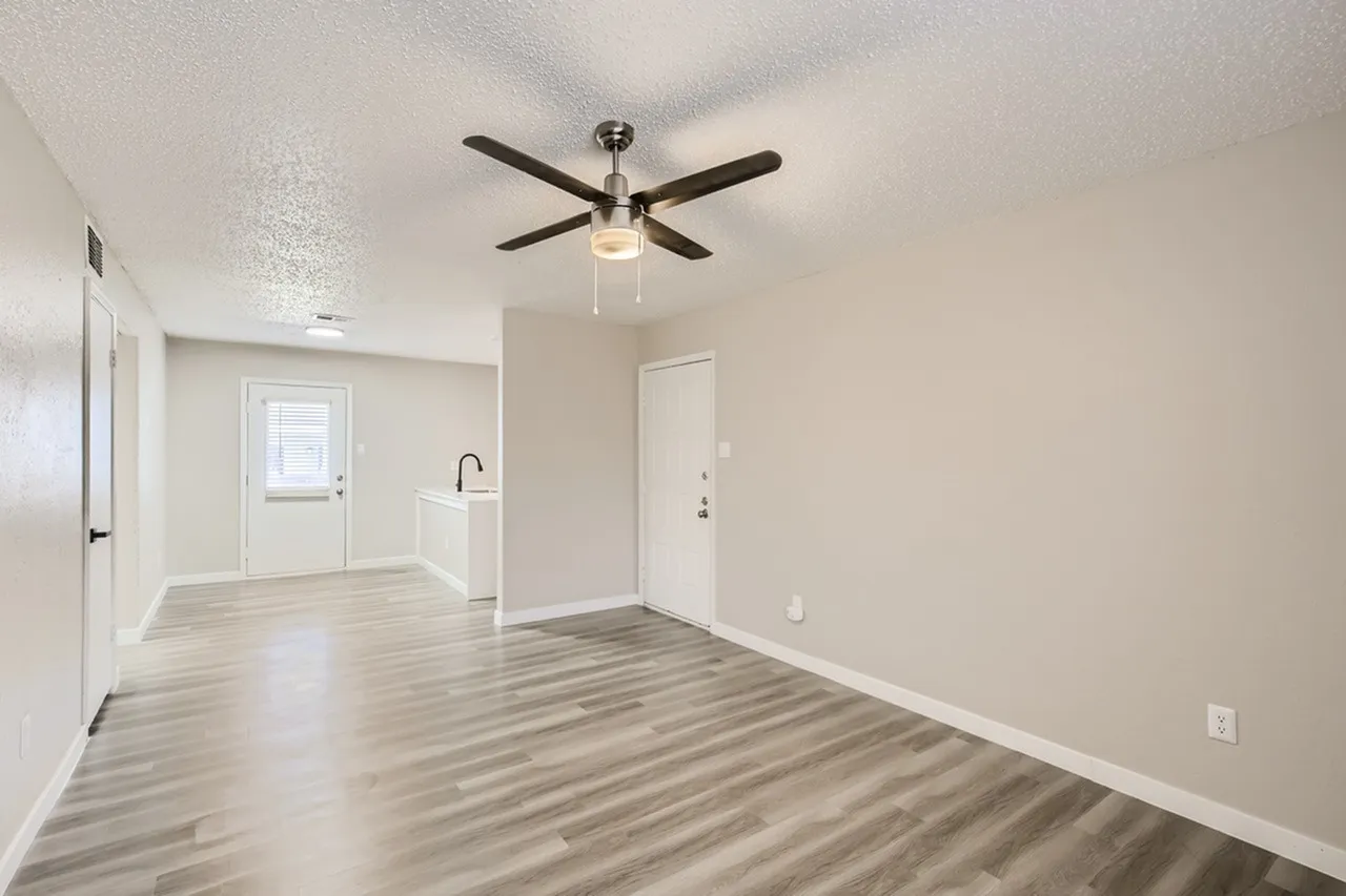Open living area, wood-style plank flooring, ceiling fan with light, white walls