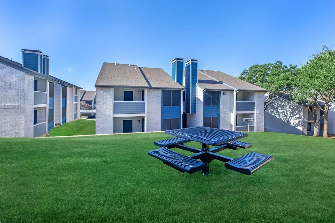 Courtyard with blue picnic table, green lawn, multi-story apartment buildings, clear sky