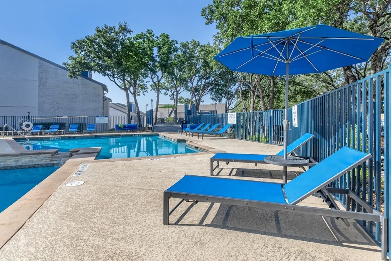 Pool area, blue lounge chairs, patio umbrella, trees, fencing