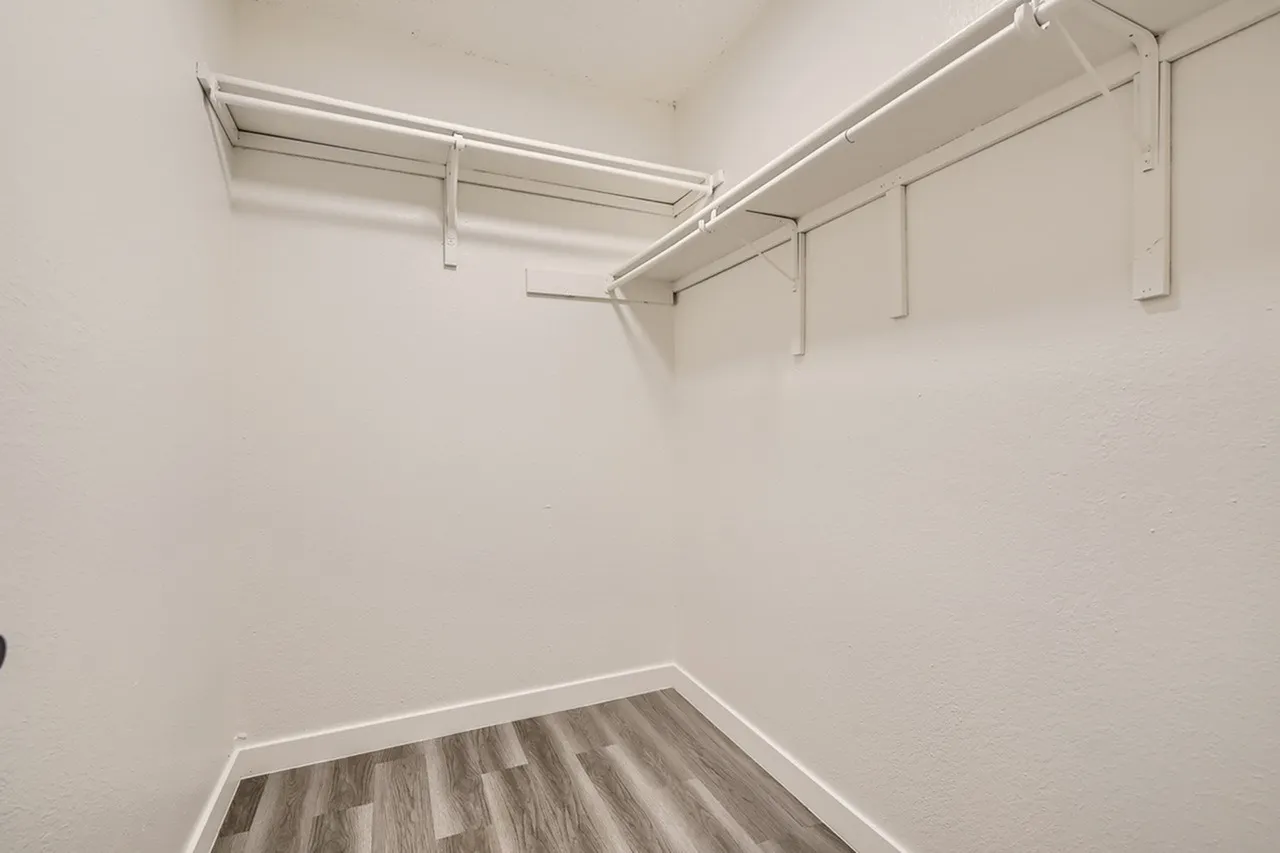 Walk-in closet, white shelving units, wood-style plank flooring, white walls, ceiling tracks
