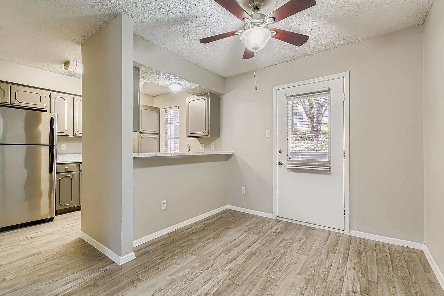 Dining area with wood-style plank flooring, ceiling fan, pass-through to kitchen with stainless appliances
