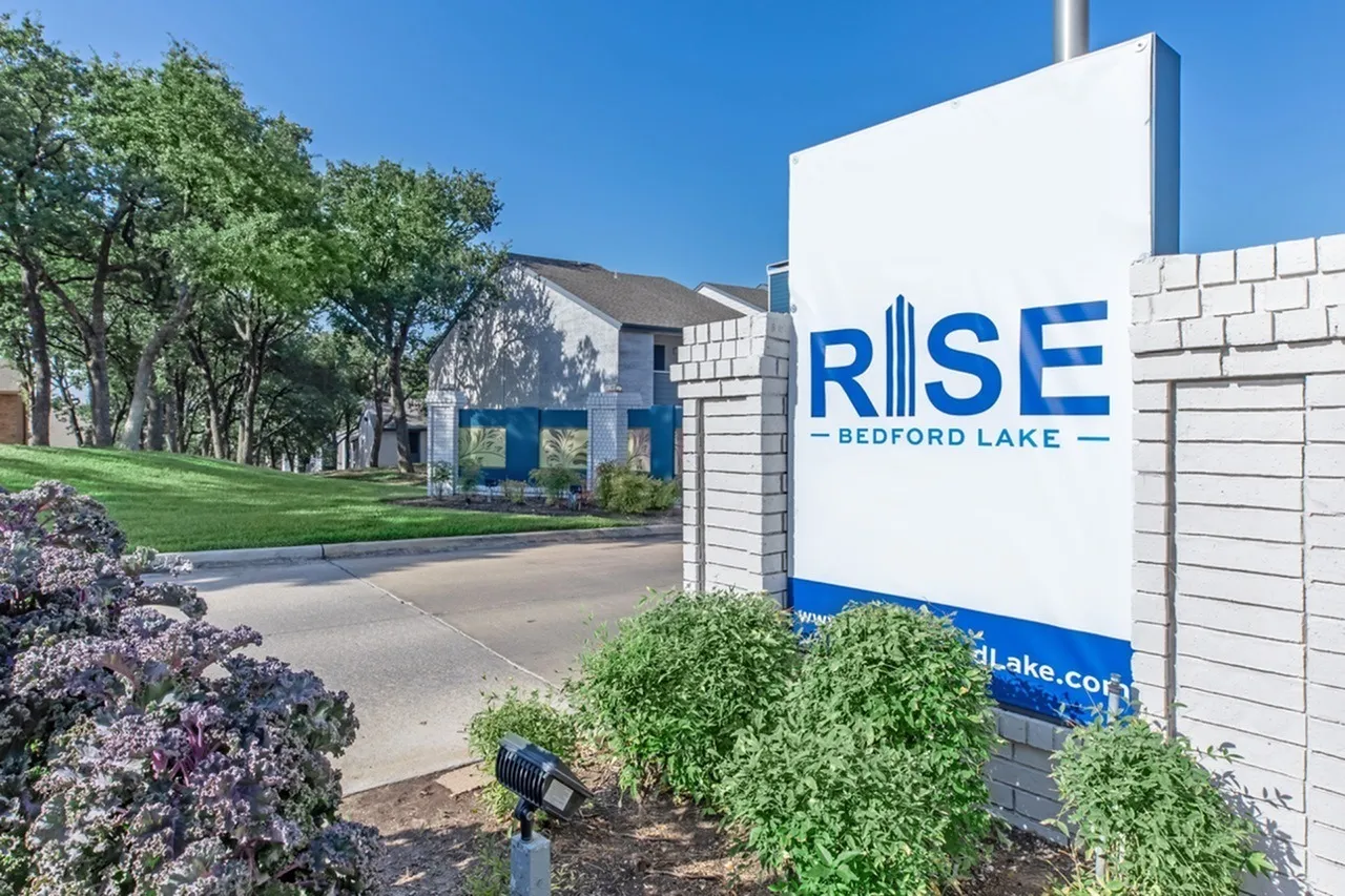 Property signage, brick construction, landscaping with flowering shrubs, green lawn, architectural building facade
