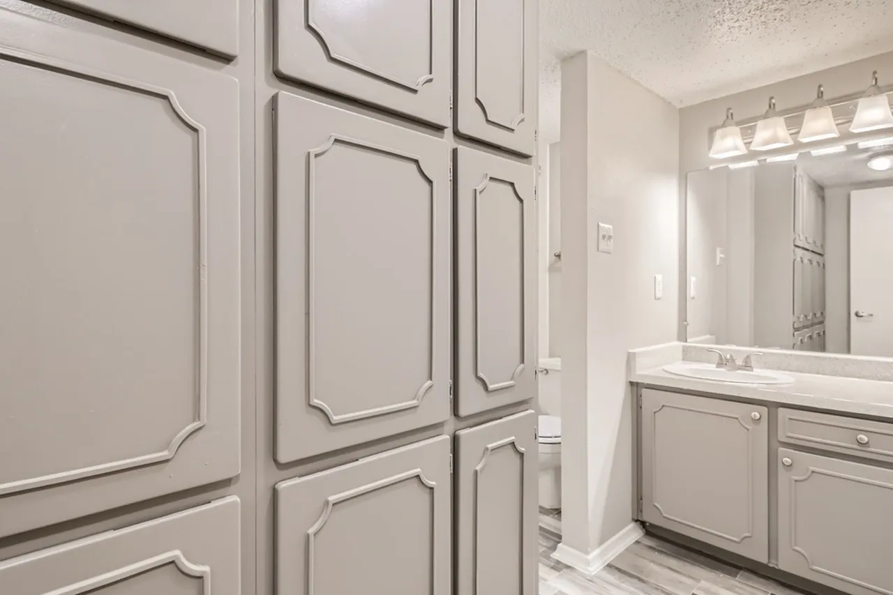 Primary bathroom, white cabinetry, quartz countertops, single vanity sink, framed mirror, chrome fixtures, wood-style plank flooring