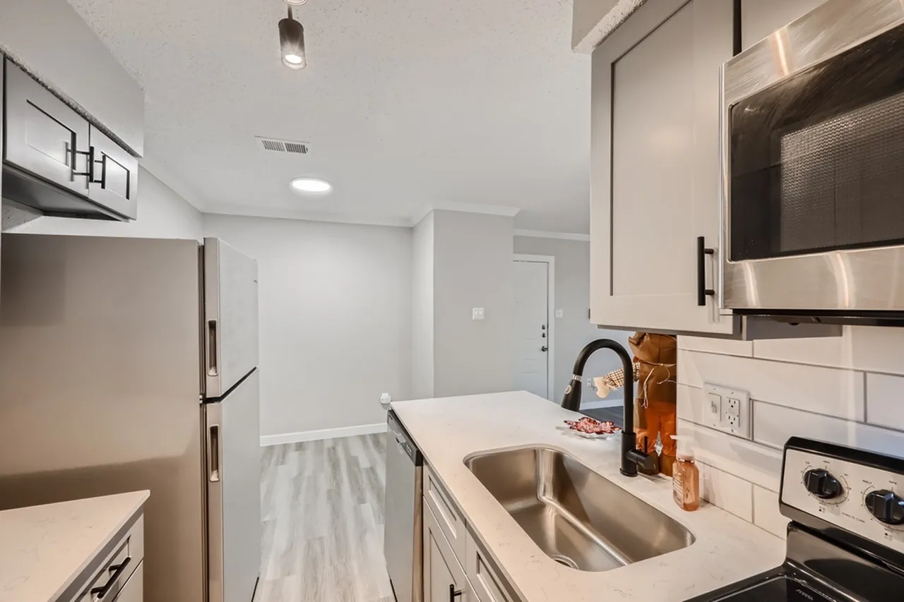 Kitchen with white cabinetry, quartz countertops, stainless appliances, wood-style plank flooring