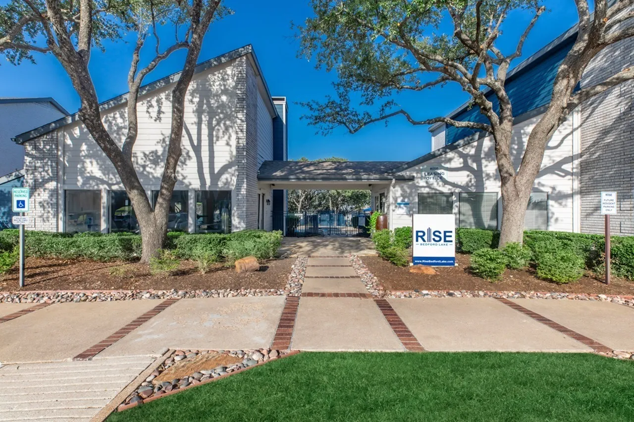 Modern residential buildings, brick and siding facade, mature trees, concrete walkway with red brick accents, landscaping, signage