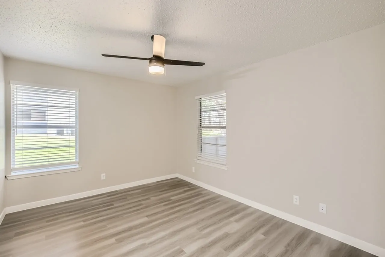 Bedroom, wood-style plank flooring, ceiling fan with light, two windows with blinds