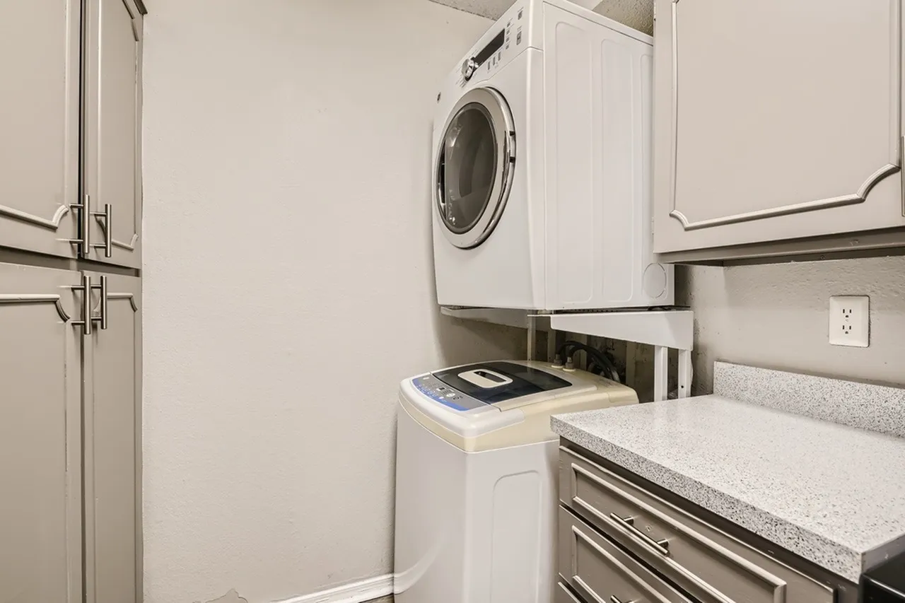 Laundry room, white front-load washer, quartz countertops, white cabinetry, tile flooring