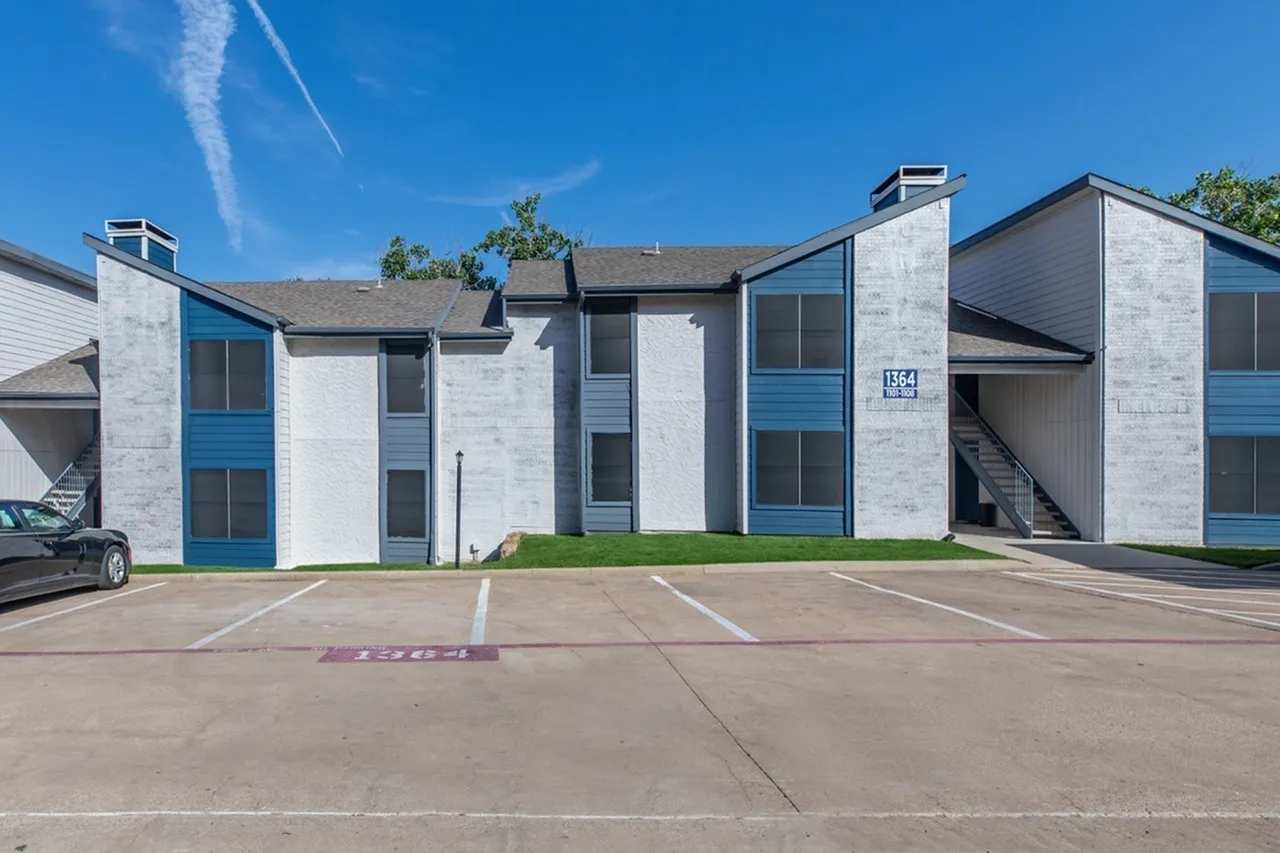 Modern residential building, white and blue facade, dark roof, parking lot, landscaping, blue sky