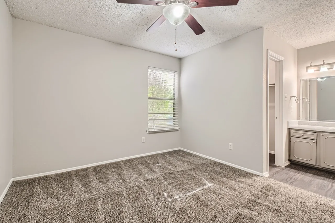 Primary bedroom, gray carpet flooring, ceiling fan, ensuite bathroom entry