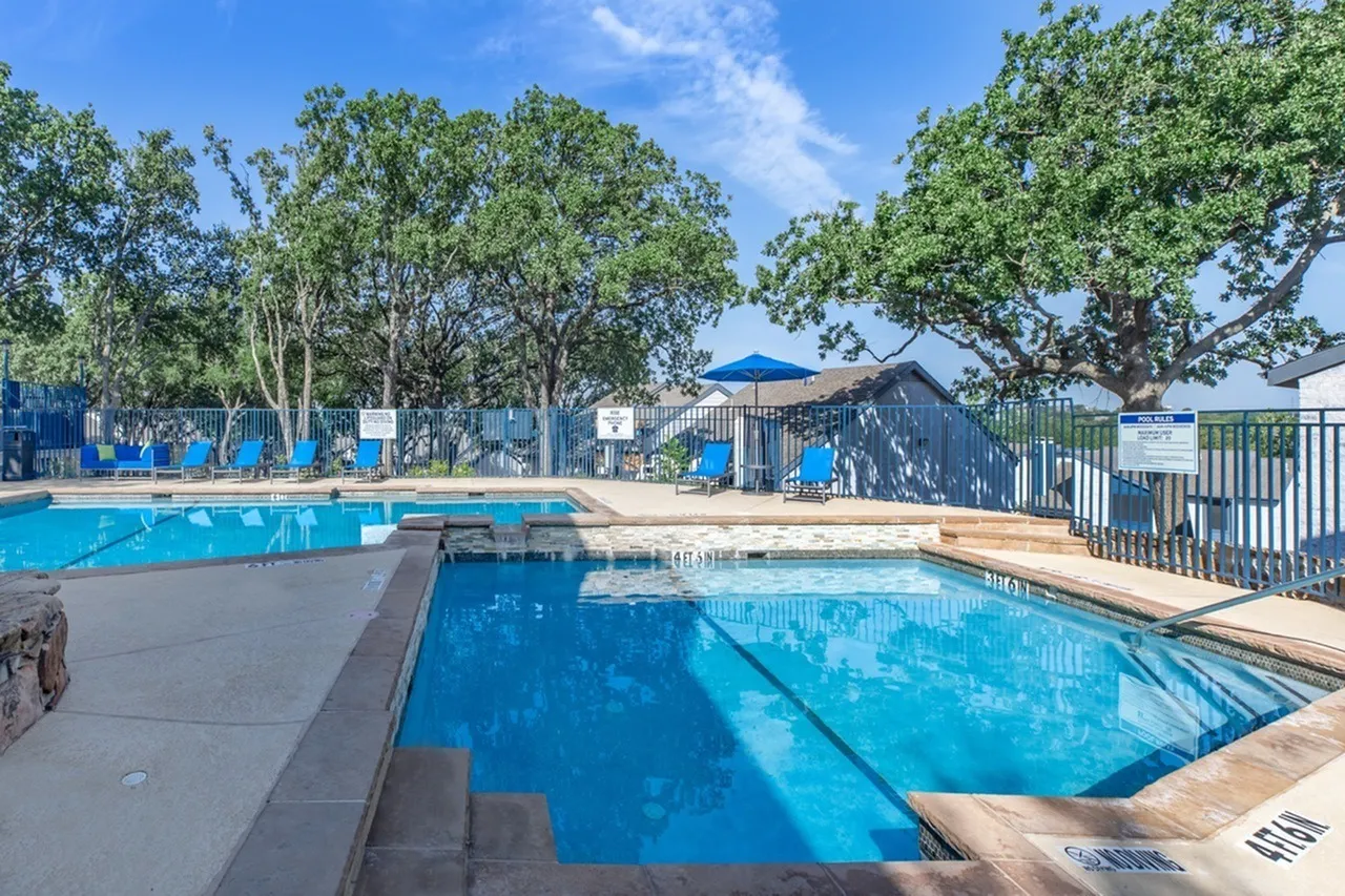 Outdoor pool area, lap pool with lane markings, spa, mature trees, blue umbrellas