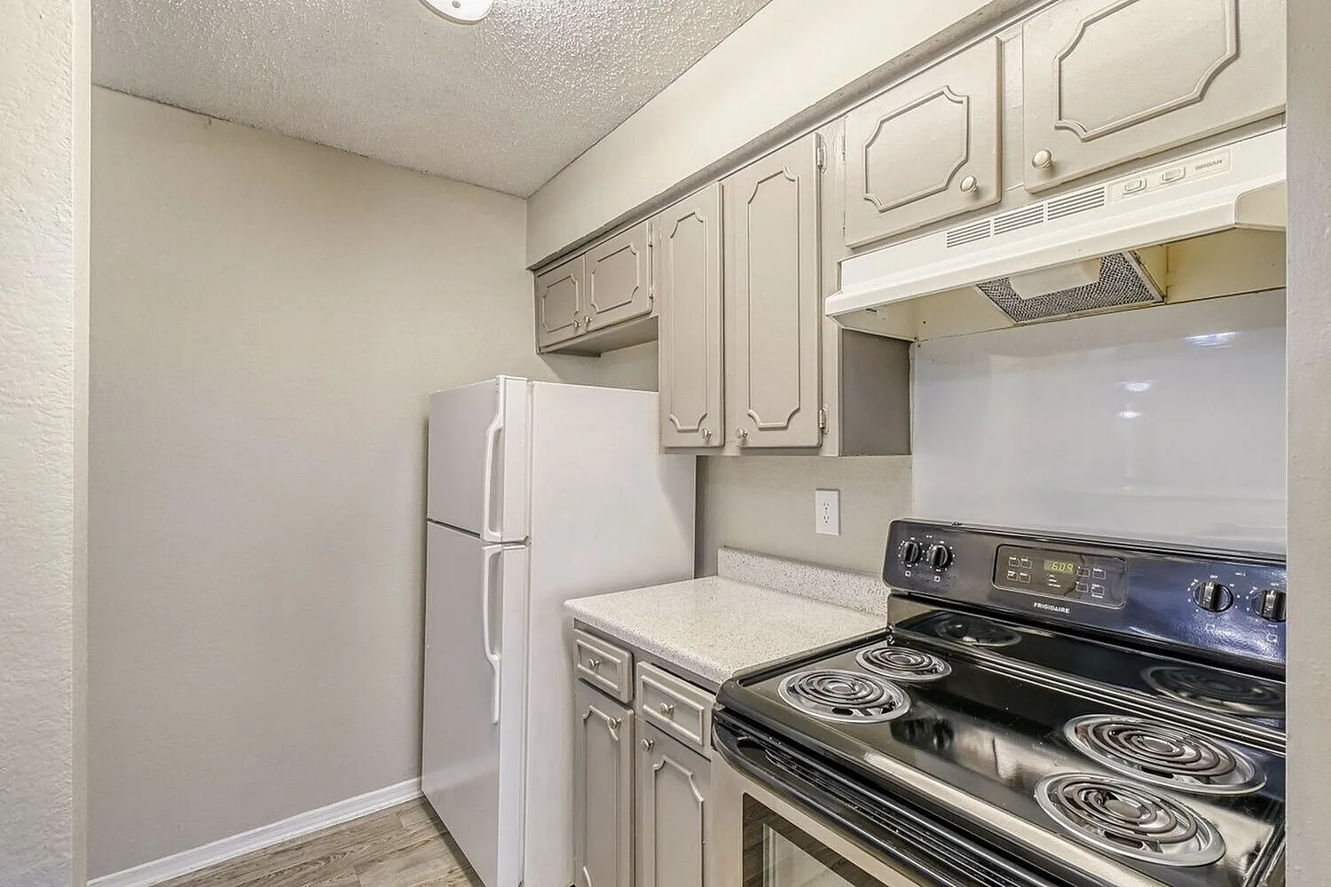 Kitchen, cream cabinetry, electric range, white refrigerator, wood-style plank flooring