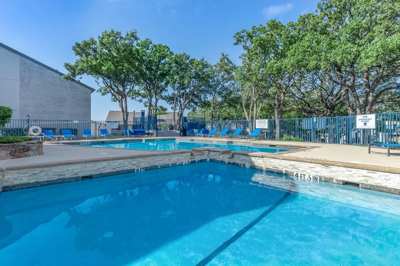 Swimming pools with lane dividers, blue fencing, mature trees, concrete deck