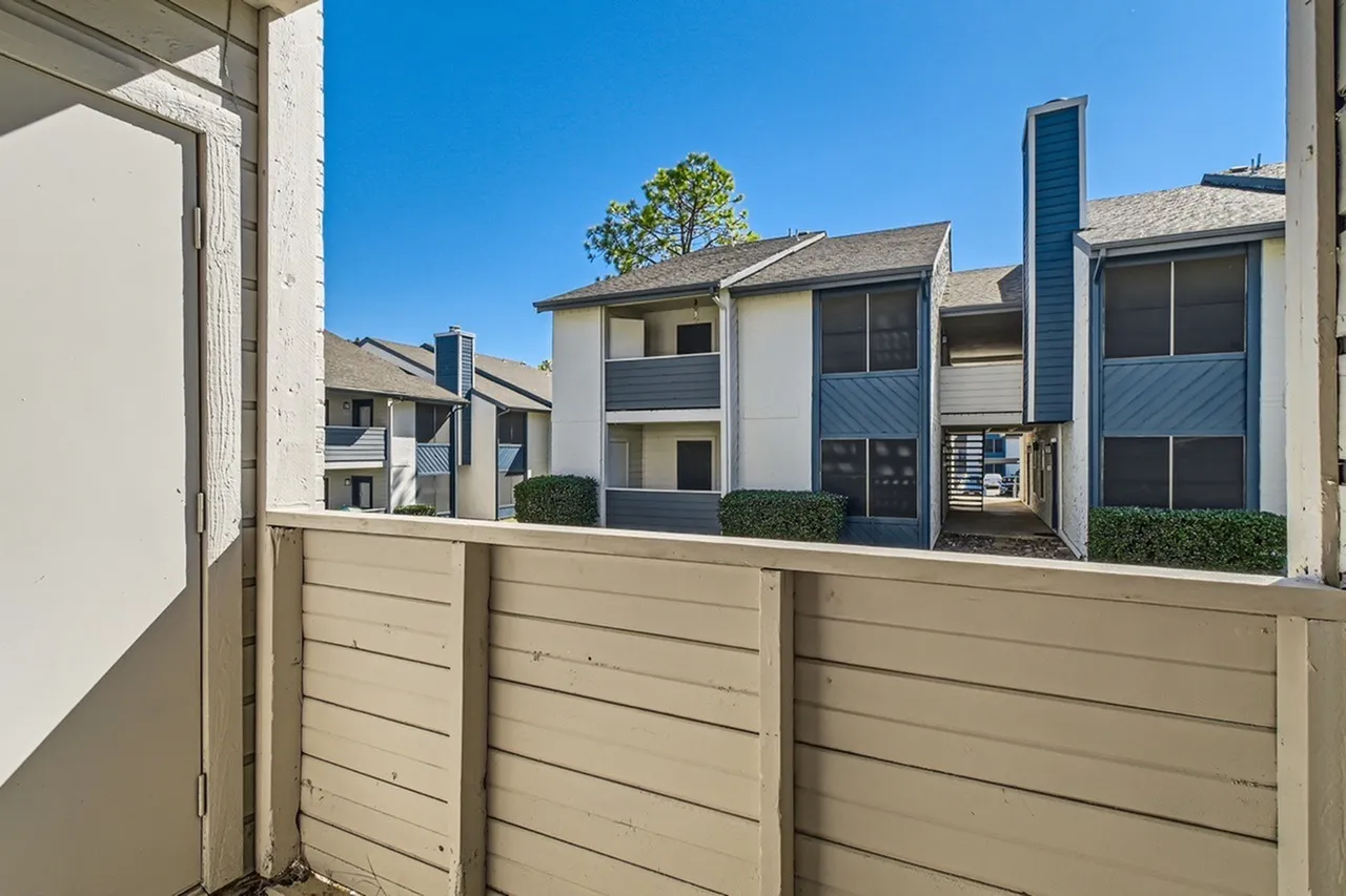 Courtyard view with tan horizontal wood fence, contemporary buildings with white and dark finishes, clear blue sky