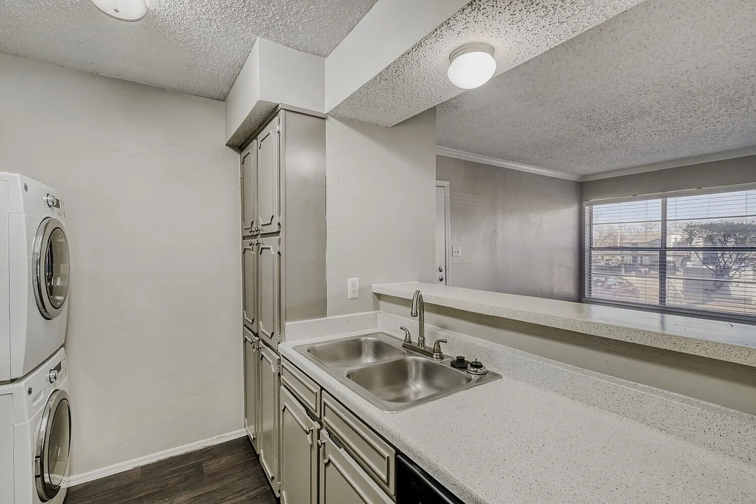 Laundry room with stacked washer and dryer, kitchen with stainless steel sink, beige cabinetry, quartz countertops, wood-style plank flooring