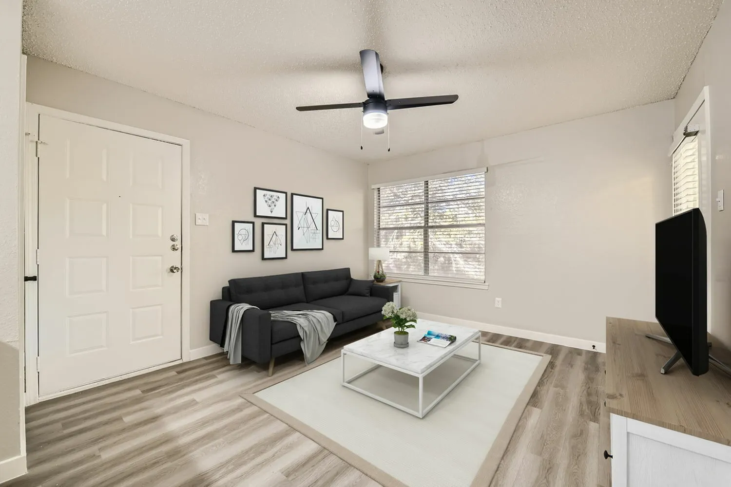Living room with wood-style plank flooring, black sofa, ceiling fan, white coffee table, framed wall art