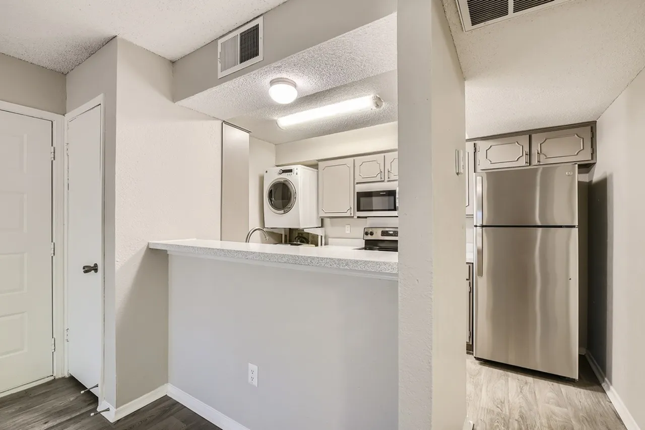 Kitchen with white cabinetry, stainless steel appliances, quartz countertops, wood-style plank flooring, washer/dryer combo, LED lighting