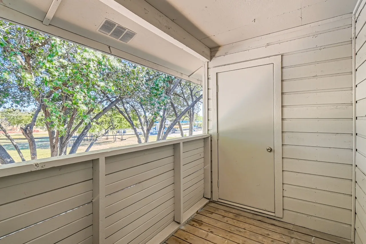 Covered patio, horizontal siding walls, wood-style plank flooring, entry door, window with tree views