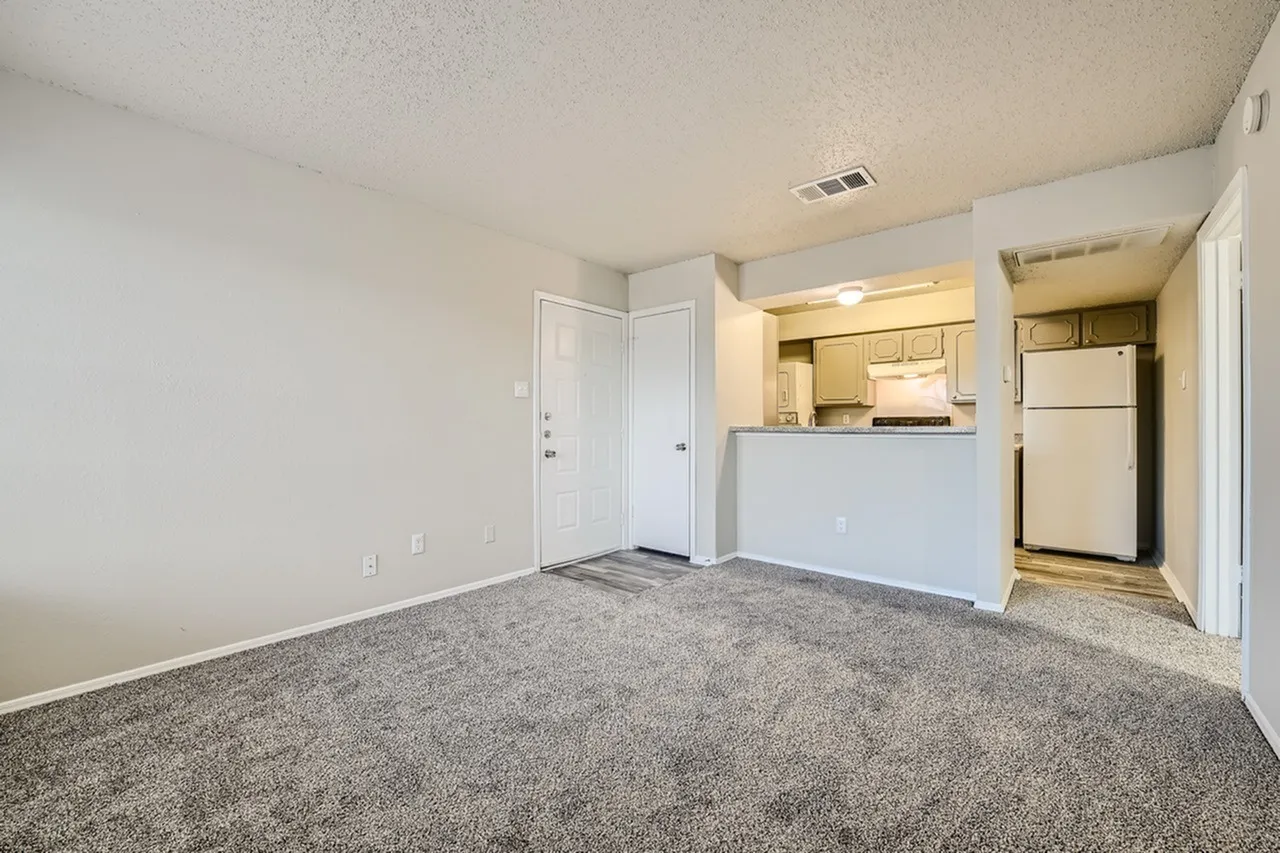 Living room with gray carpet, white bi-fold closet doors, kitchen with white appliances and cabinetry