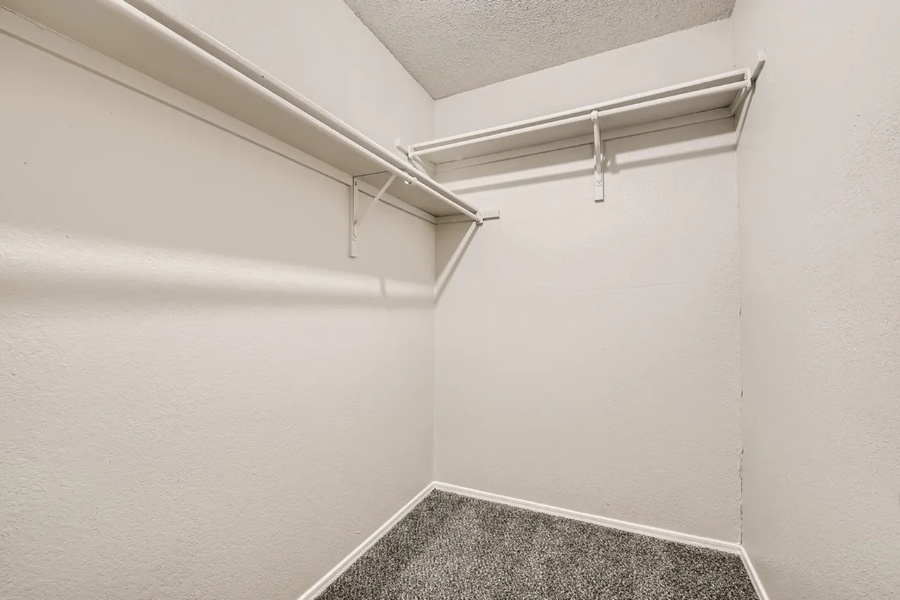 Walk-in closet, metal shelving rods, carpet flooring, white walls