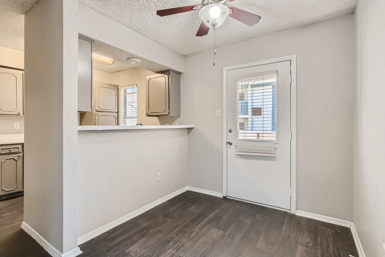 Kitchen with pass-through window, wood-style plank flooring, white door with window, ceiling fan