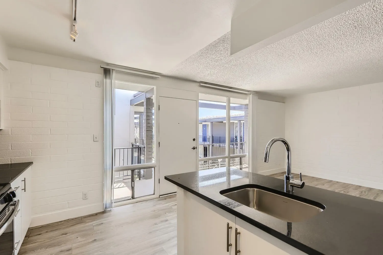 Kitchen, black quartz countertops, stainless steel sink, wood-style plank flooring, glass sliding doors to balcony