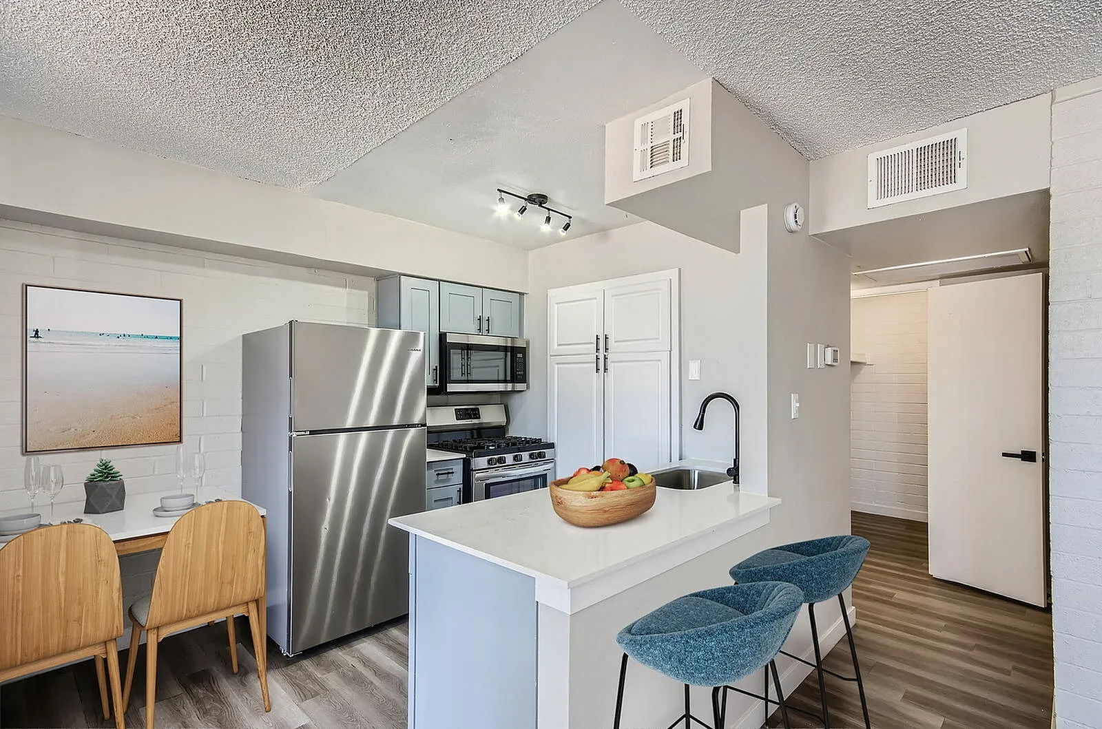 Kitchen with white cabinetry, quartz countertops, stainless appliances, wood-style plank flooring, island seating