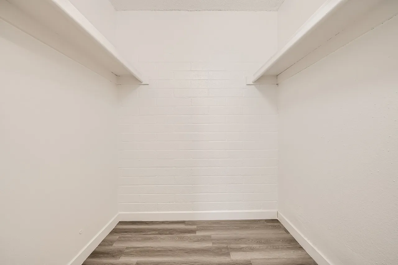 Closet, white shaker-style walls, wood-style plank flooring, built-in shelving above
