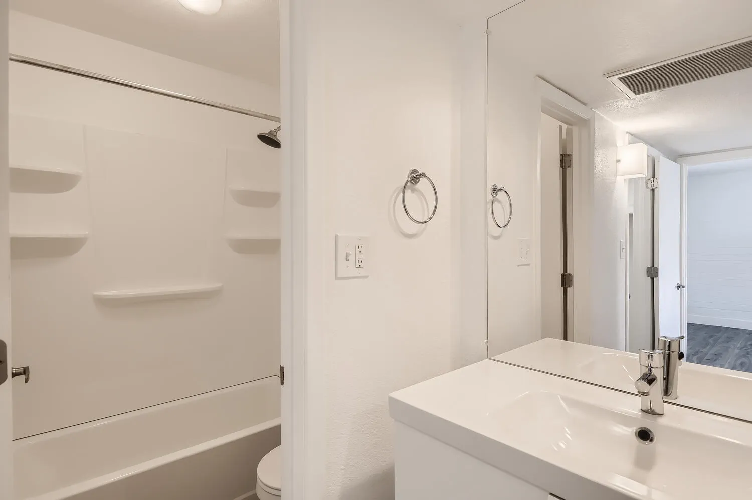 Bathroom, white vanity with sink faucet, large mirror, chrome towel rings, shower tub with enclosure