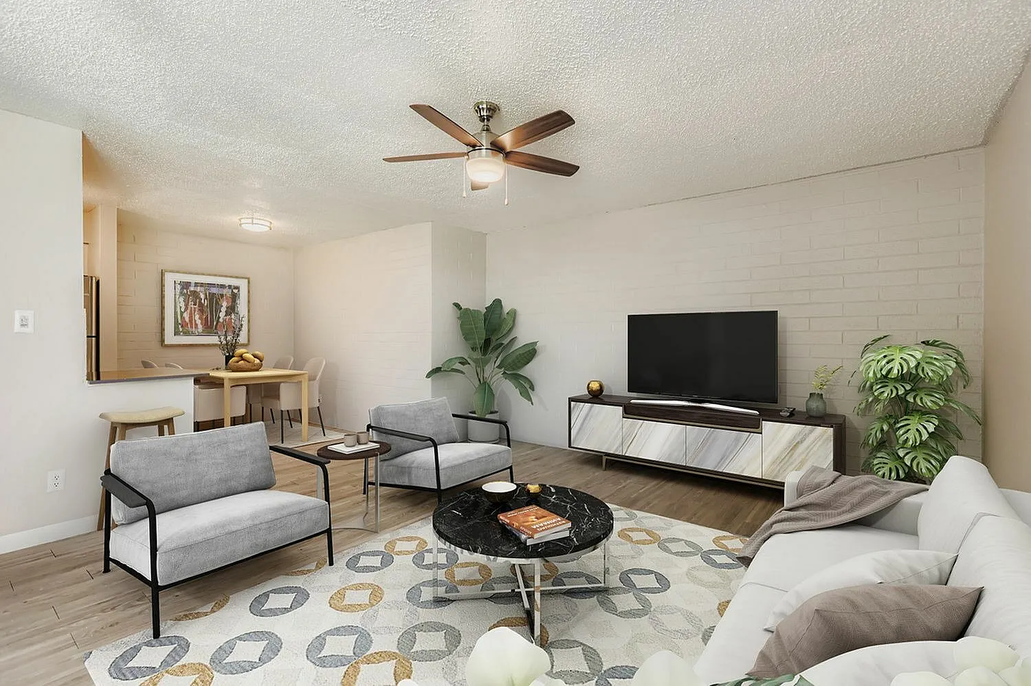 Living room with wood-style plank flooring, ceiling fan, gray upholstered seating, TV on media console, potted plants