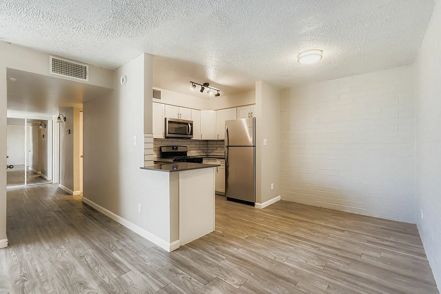 Kitchen, stainless steel appliances, striped backsplash, wood-style plank flooring, white cabinetry