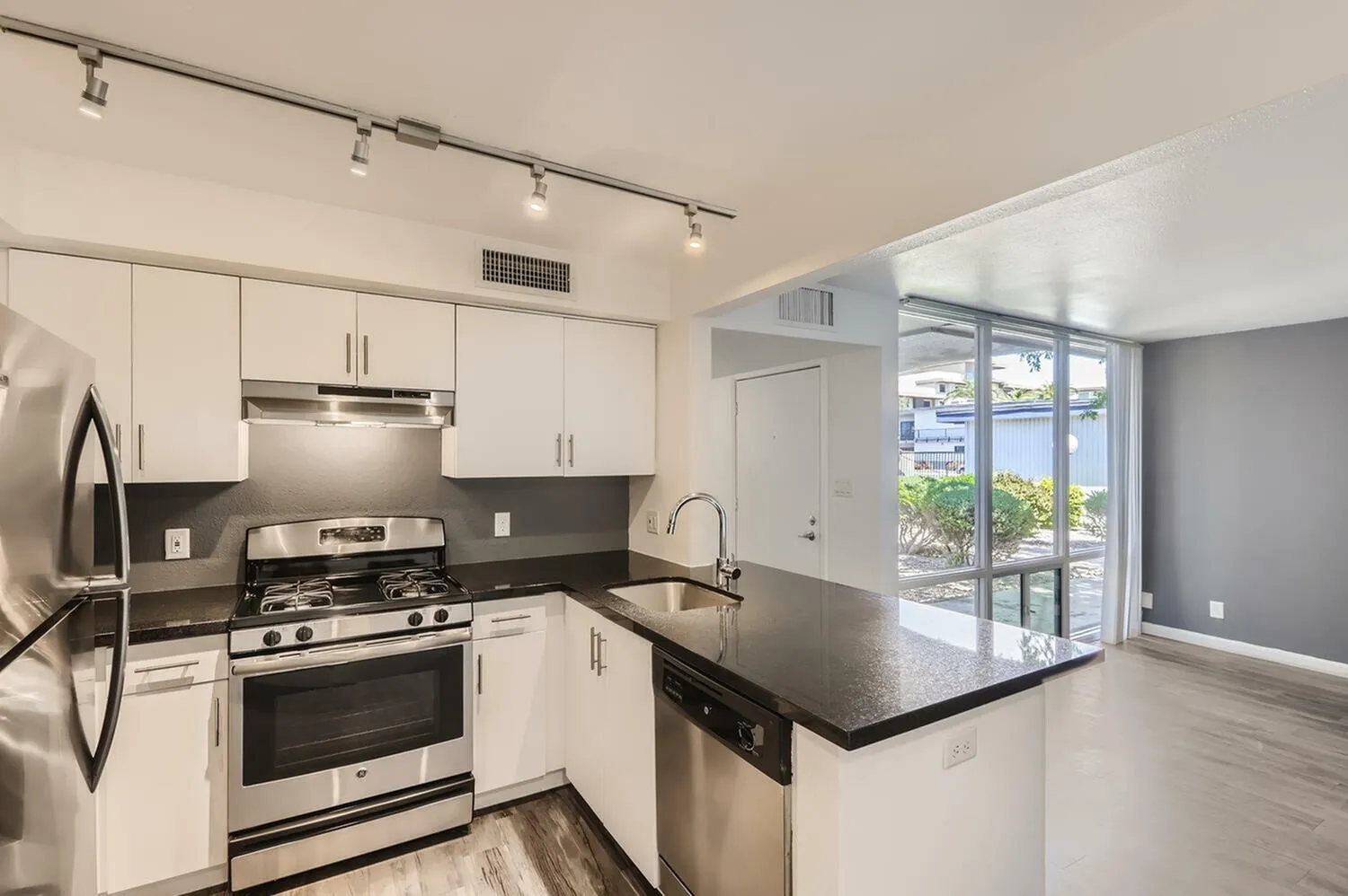 Kitchen, white shaker cabinetry, black countertops, stainless steel appliances, wood-style plank flooring