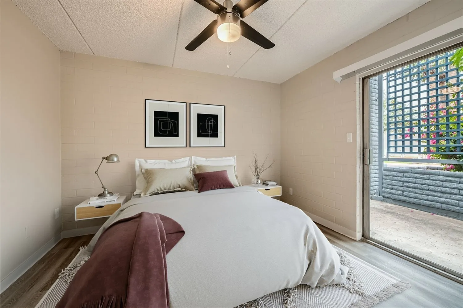 Primary bedroom, wood-style plank flooring, ceiling fan, glass patio door, bedside nightstand with lamp