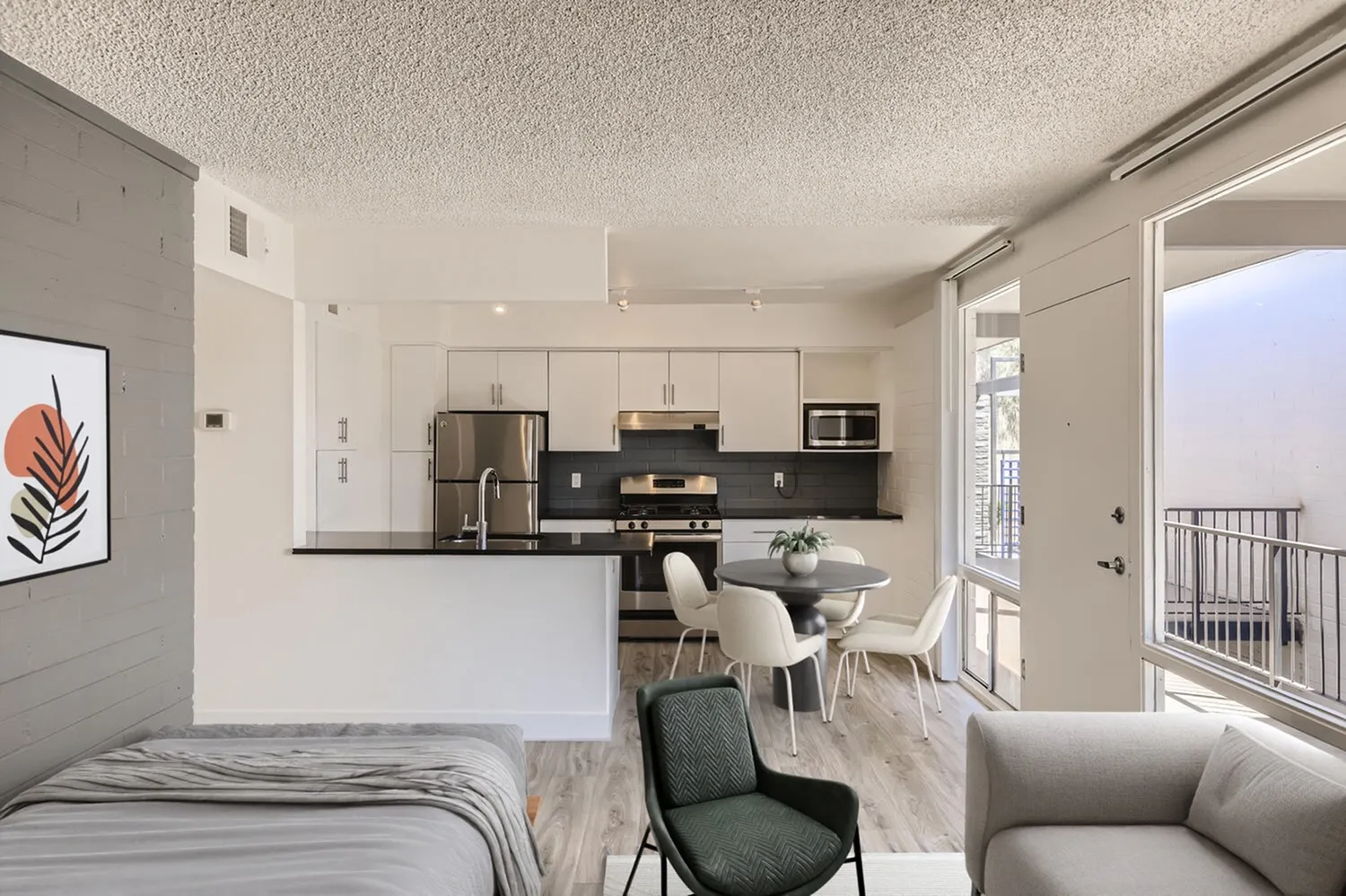 Studio, open concept kitchen with white cabinetry, black countertops, stainless appliances, wood-style plank flooring, balcony access