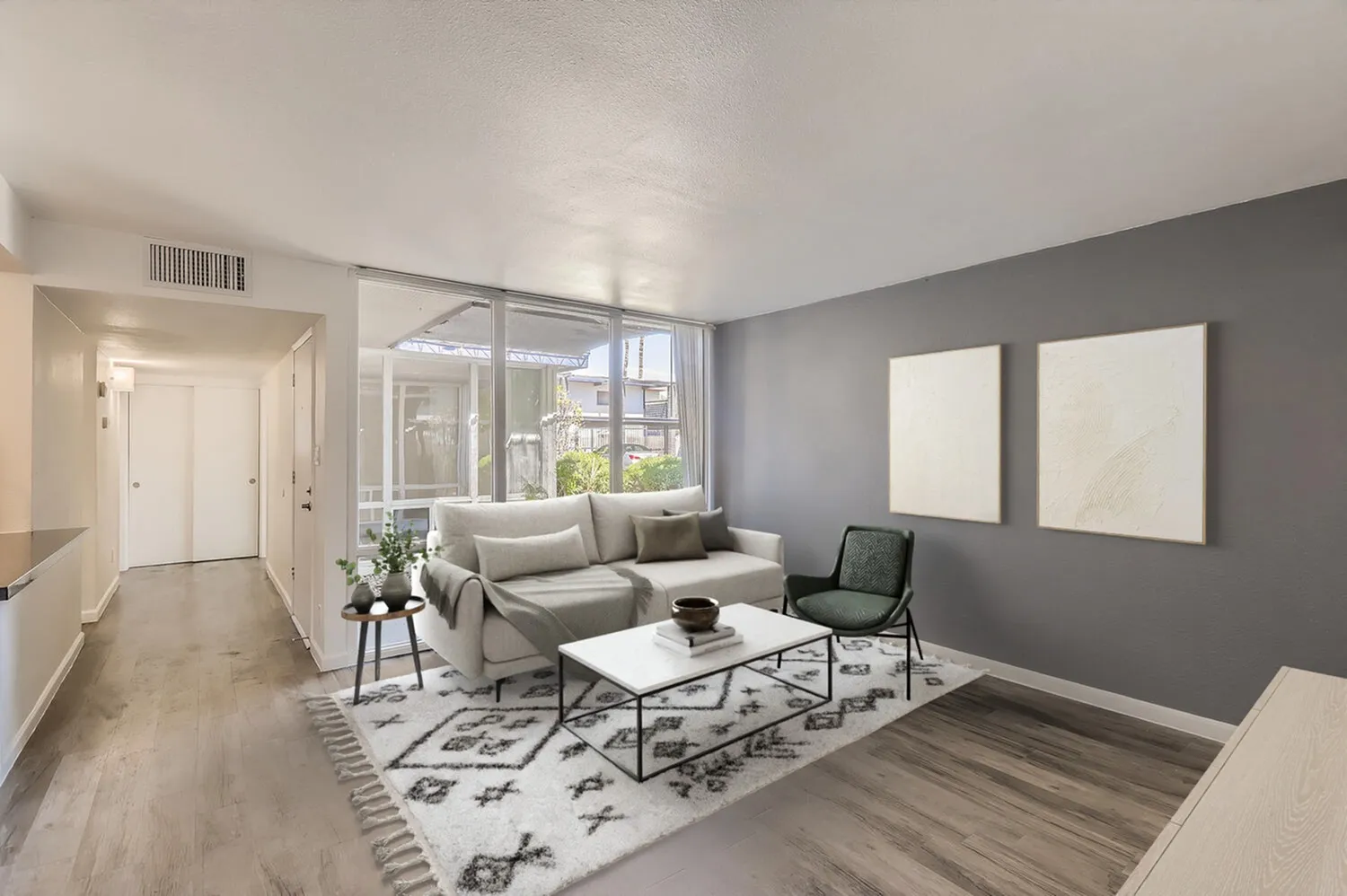 Living room with gray walls, wood-style plank flooring, gray sofa, white coffee table, large windows with natural light