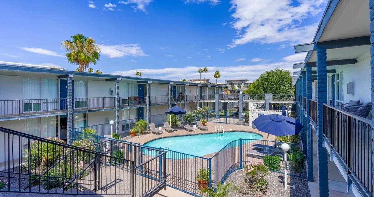 Pool, lounge chairs, palm trees, blue umbrellas, multi-story apartments